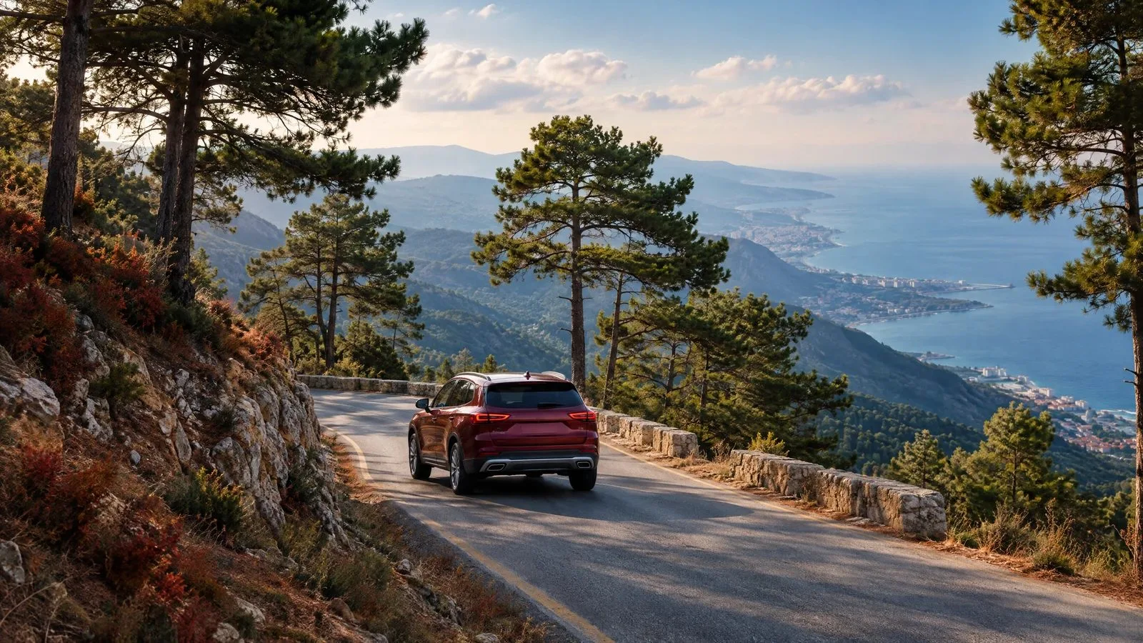 A pine-lined mountain road overlooks the distant Mediterranean coast.